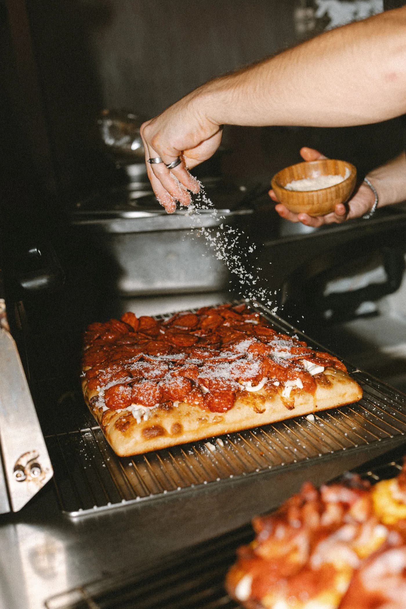 Fresh parmesan being sprinkled over a hot Pepperoni pizza straight out of the oven